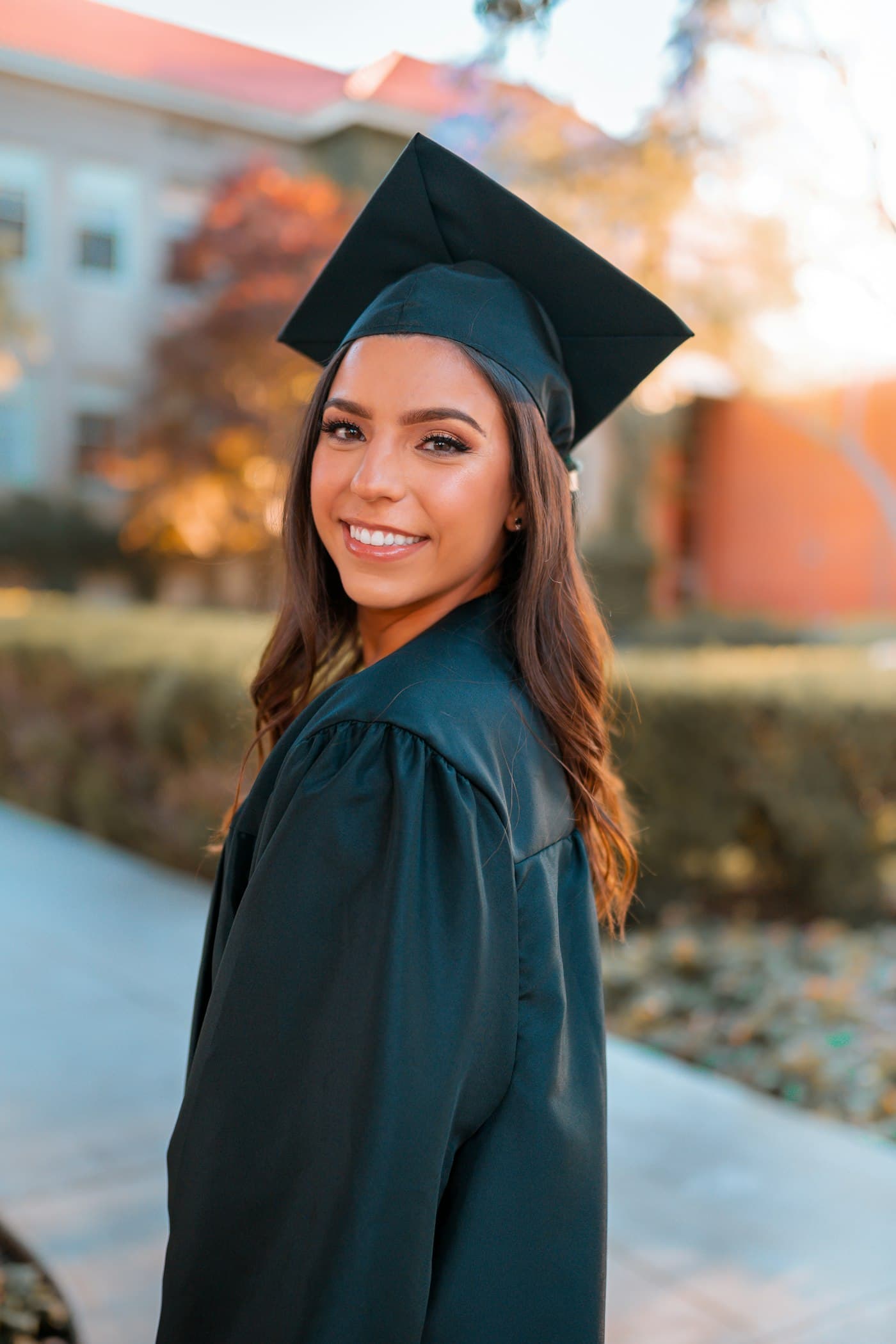 A graduate in cap and gown smiling on a sunlit campus